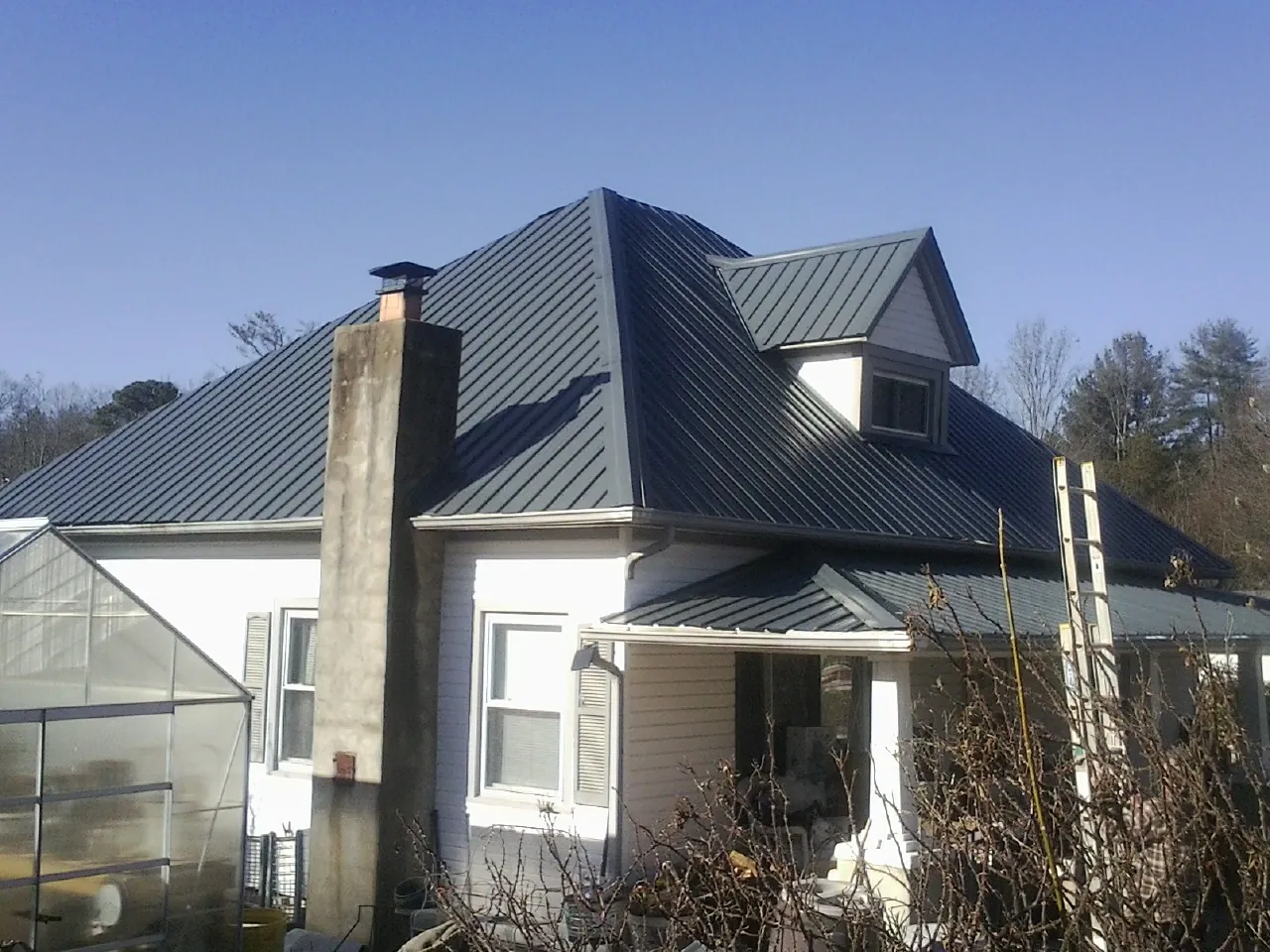 Dark blue standing seam metal roof on a white farmhouse with dormer — Slate & Tile Roof Repair by Roofing Brothers in Millport
