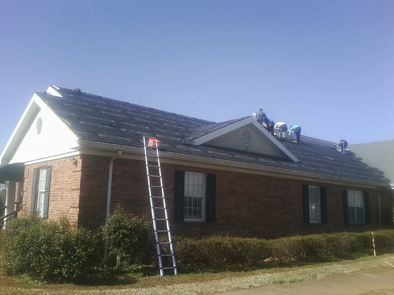 Crew tearing shingles off a brick ranch roof with a ladder set — Metal Roof Repair work by our crew in Millport
