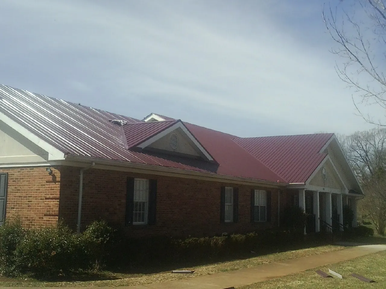 Red metal roof with gabled entries on a long brick building, from a Hail Damage Roof Repair job in Millport
