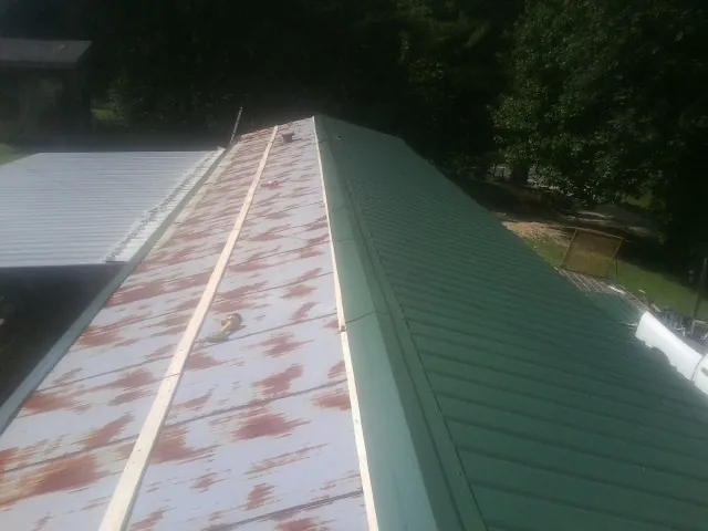 Old rusted panels beside newly installed green metal roofing — Wind Damage Roof Repair by Roofing Brothers in Millport