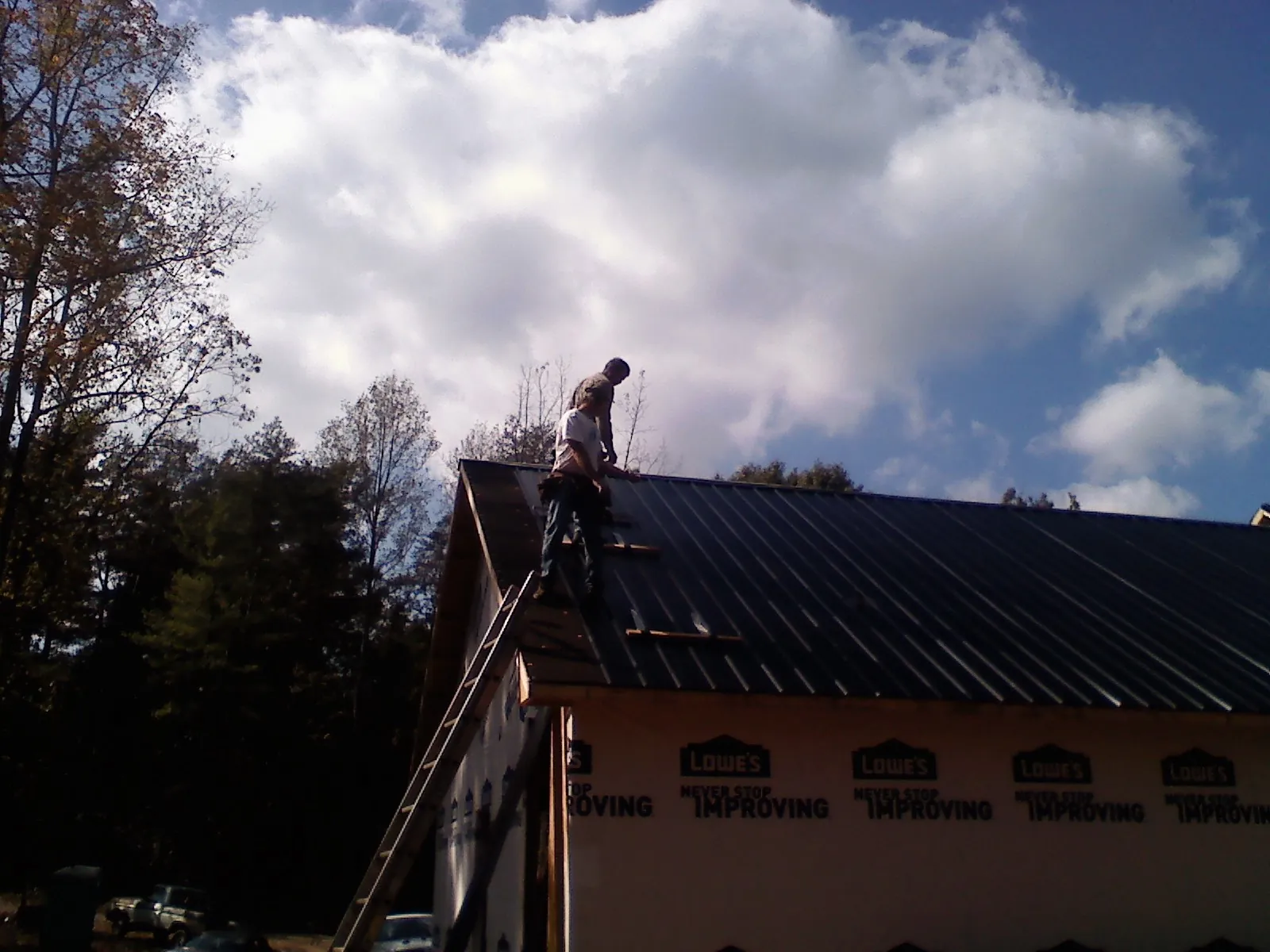 Roofer fastening dark metal panels high against a cloudy sky, from a Roof Inspection job in Millport