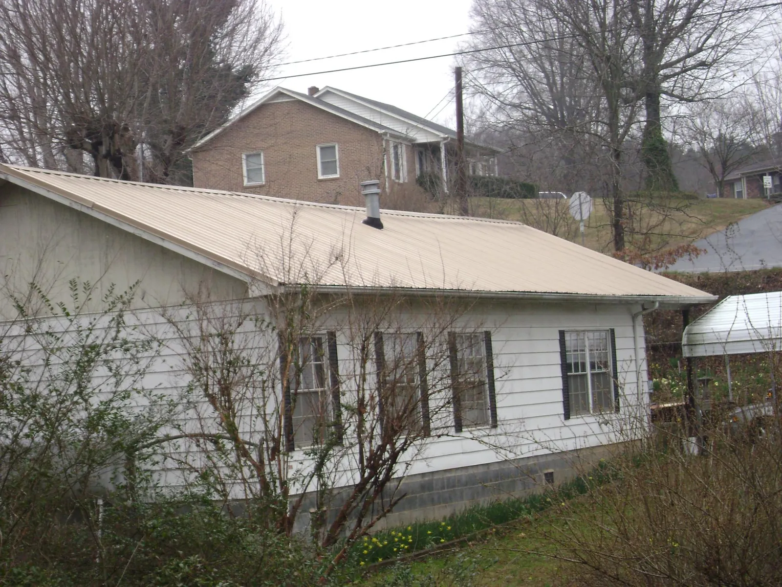 Tan metal roof on a white sided house set into a hillside — Commercial Roofing by Roofing Brothers in Millport